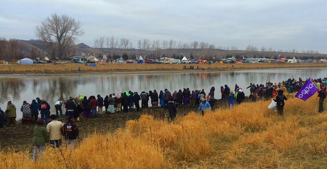 People beside a river with tents and cars