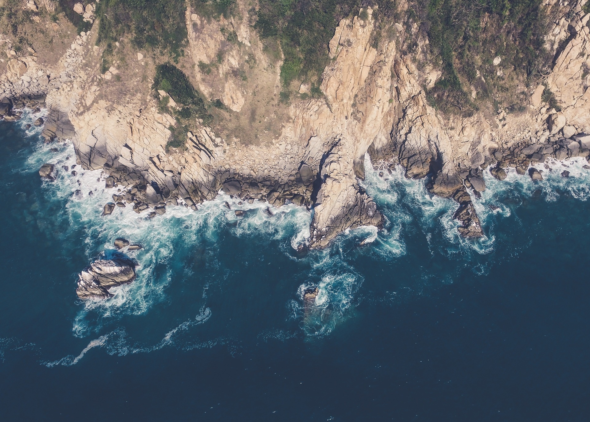 Aerial view of rocky coastline with waves crashing against cliffs and deep blue ocean