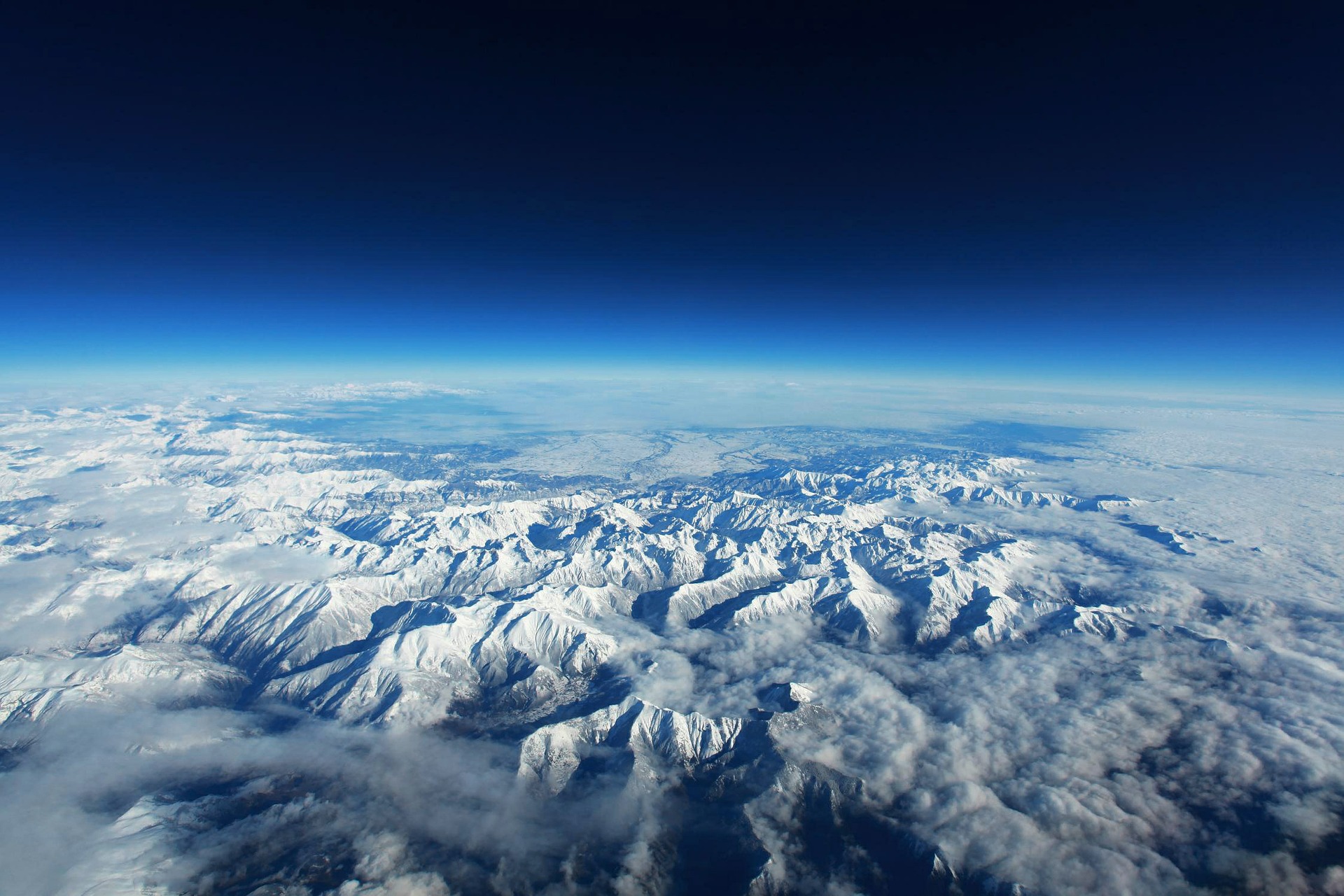 Aerial view of snow-covered mountain range with clouds and blue sky horizon