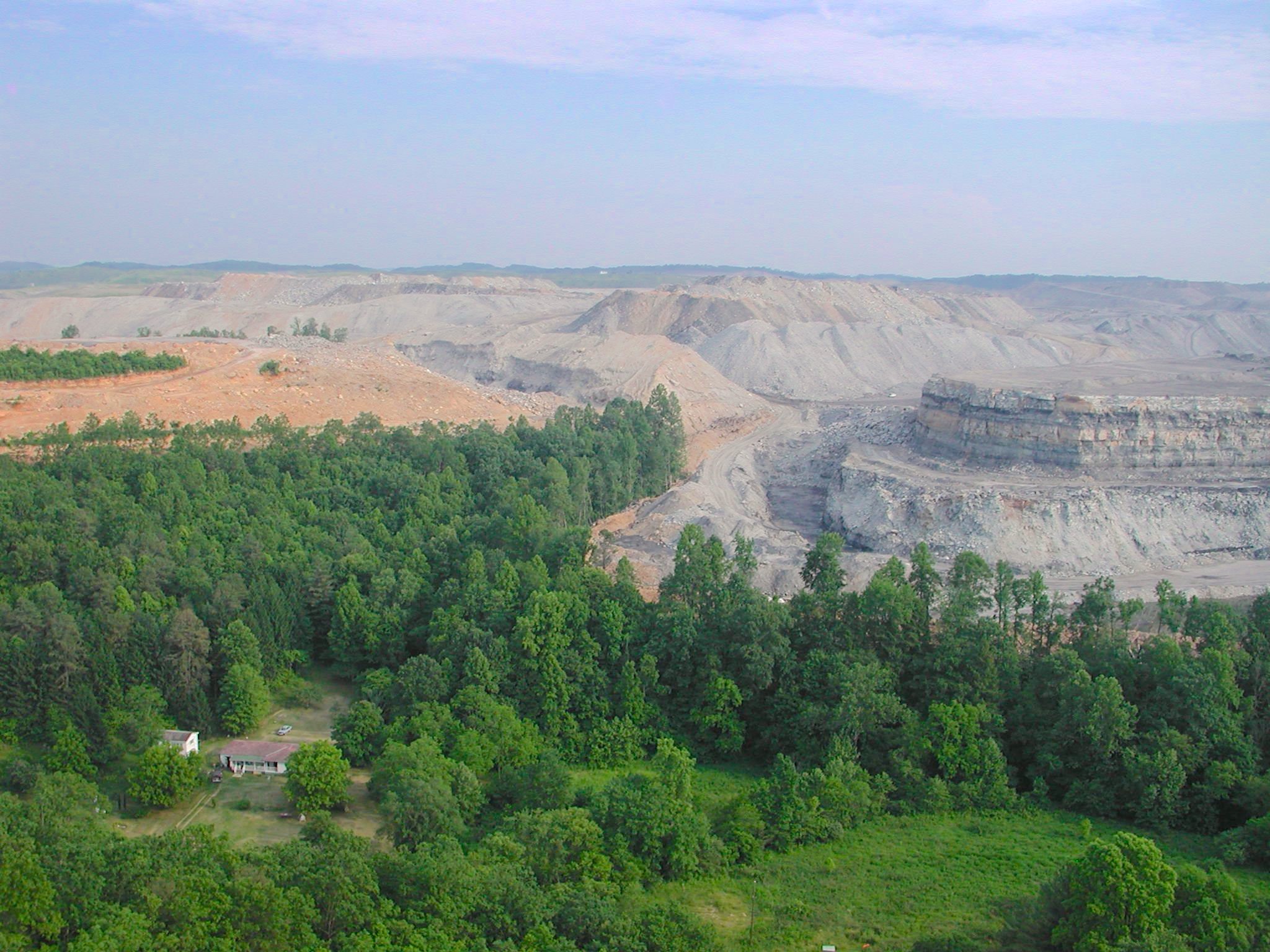 Open pit mining near forest and rural home, landscape altered by excavation